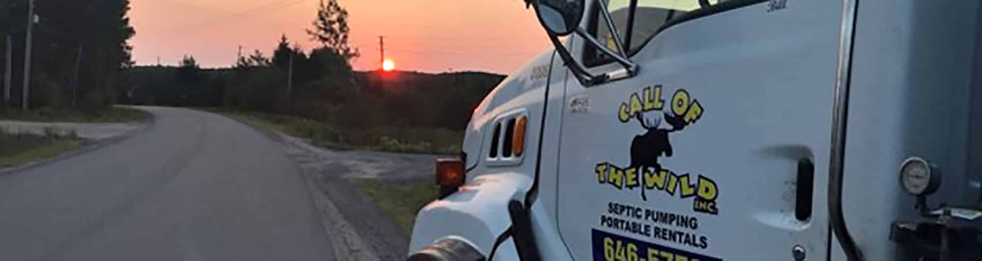 Septic pumping truck on rural road at sunset