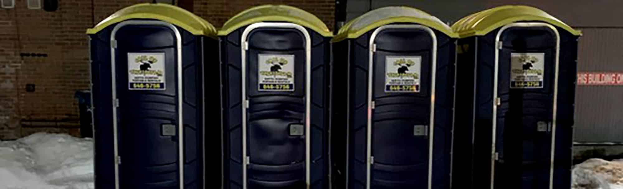 Row of four dark blue portable toilets with yellow roofs in snowy area