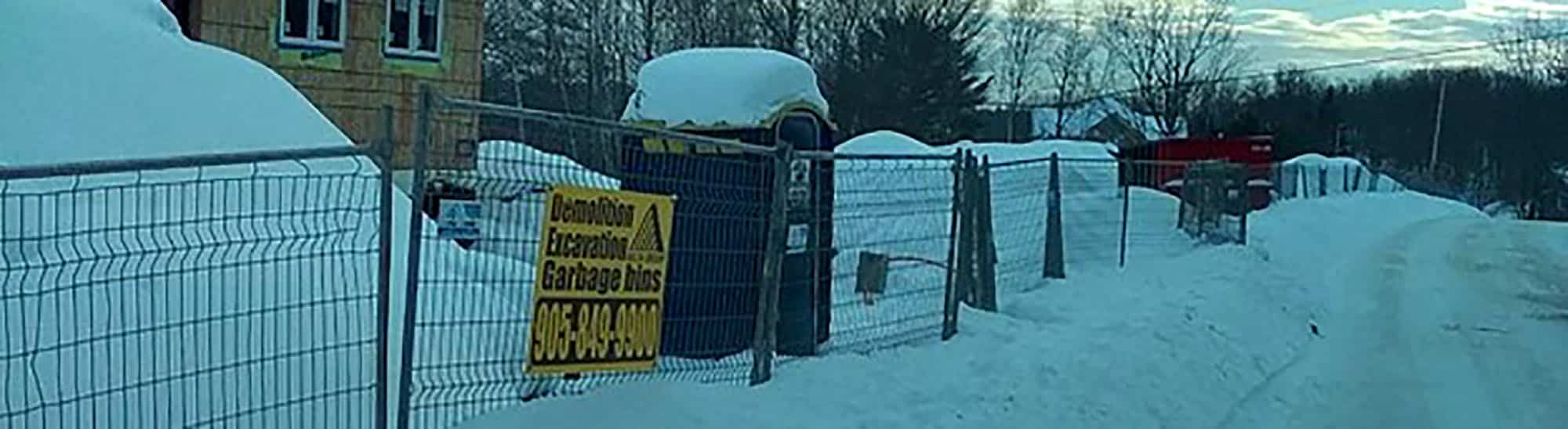 Snow-covered road near construction site with caution sign and fences