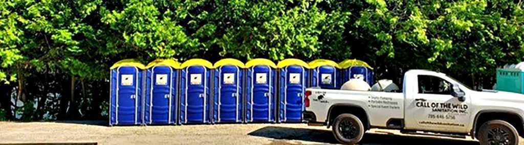 Row of blue portable toilets next to a white truck in a green outdoor setting