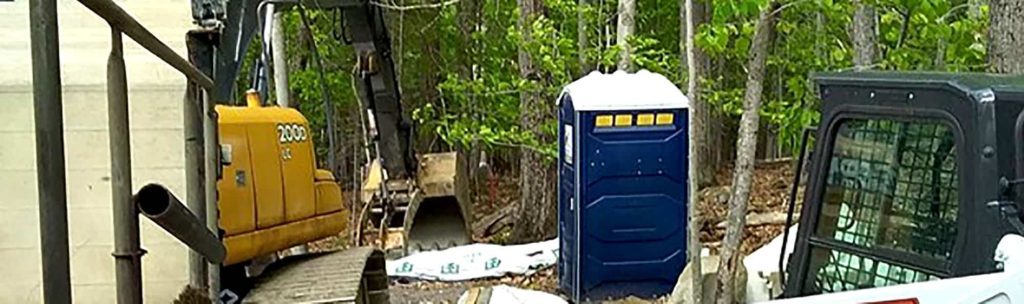 Construction site with excavator, portable toilet, and wooded area