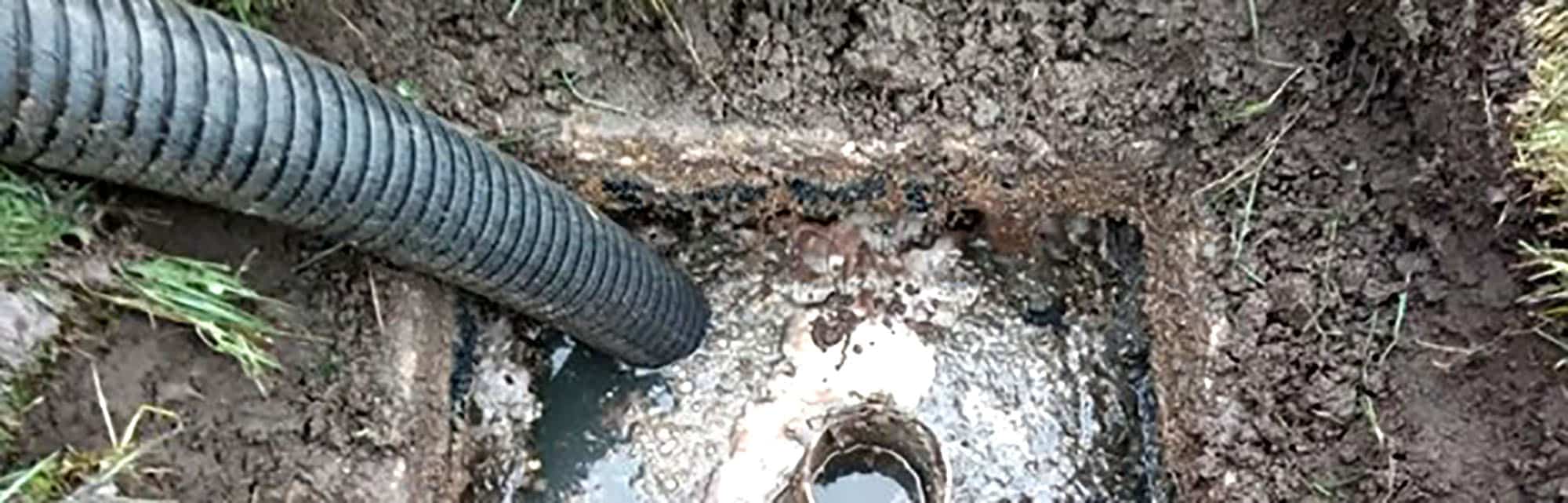 Black drainage pipe connected to a muddy outdoor ground septic system