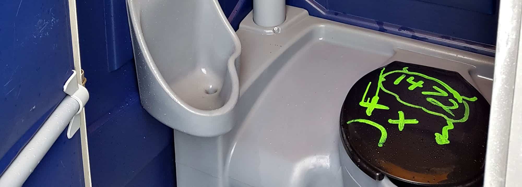 Porta potty with urinal and graffiti on toilet seat
