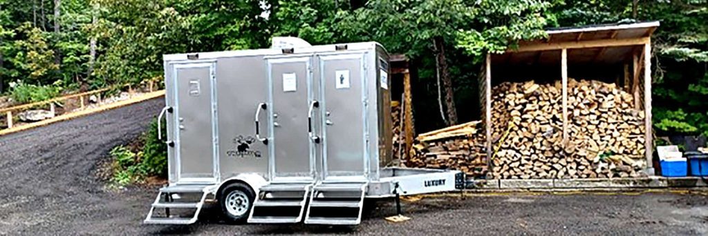 Portable restroom trailer beside woodpile in rural setting