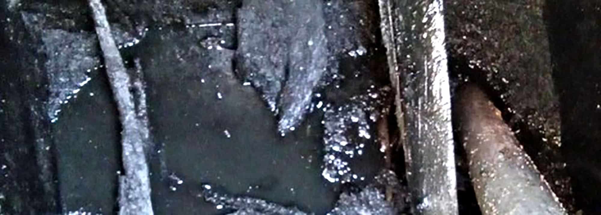 Corroded interior of septic tank surrounded by thick black residue