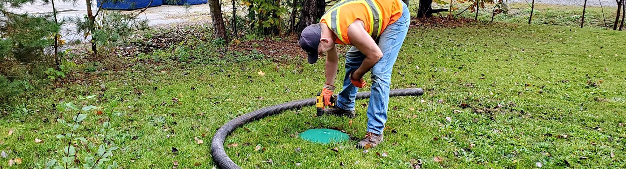 Worker inspecting septic tank in a grassy area