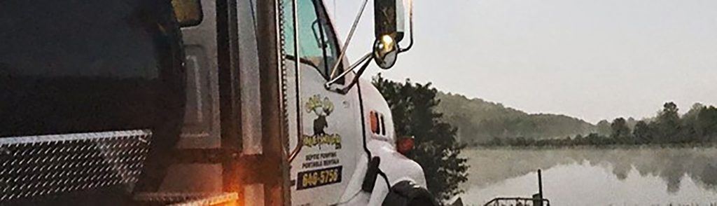 Septic service truck parked by a serene lakeside at dawn