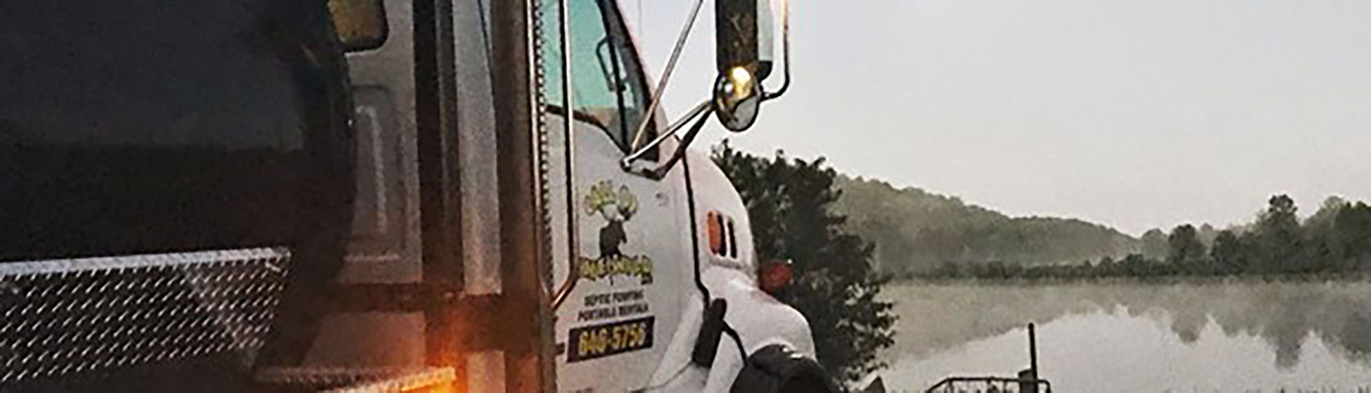 Septic service truck parked by a serene lakeside at dawn