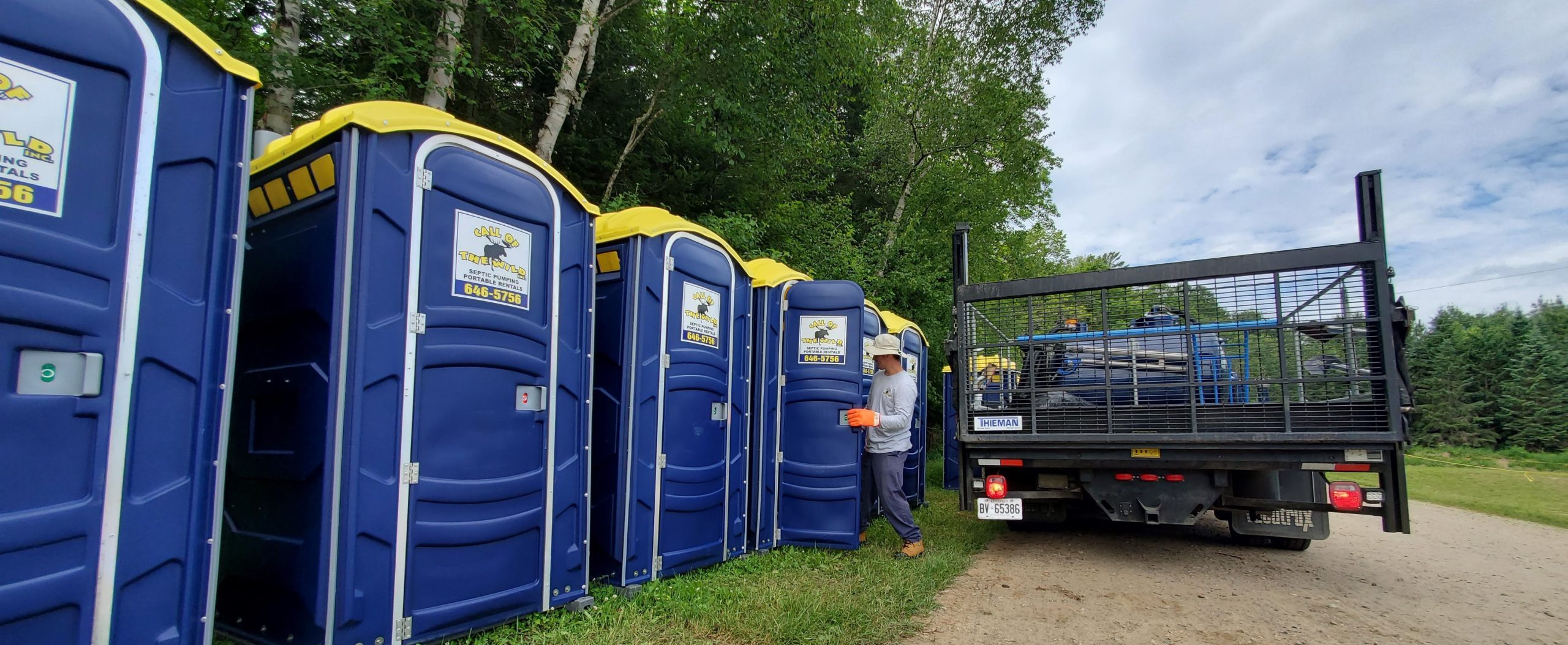 Portable toilets being serviced by a worker and truck near a forested area
